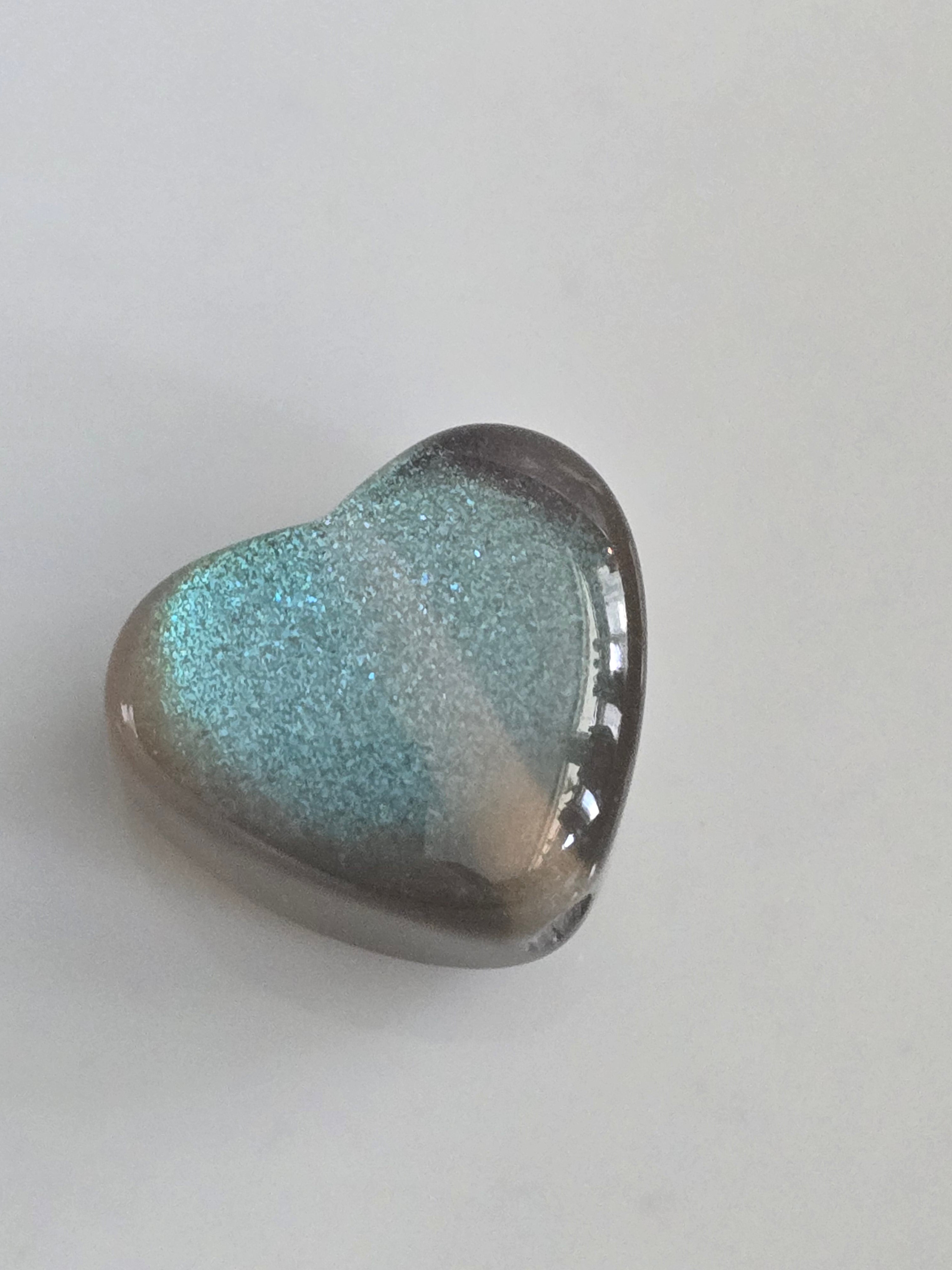 A heart-shaped resin bead featuring a glittery light blue and grey