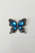 A butterfly-shaped flatback featuring large faceted blue rhinestones in the centre and smaller blue and smoky grey rhinestones set in a silver-tone.