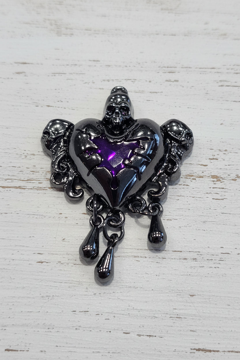 A gothic-style heart pendant featuring a central purple crystal surrounded by dark gunmetal gray skull and wing details.