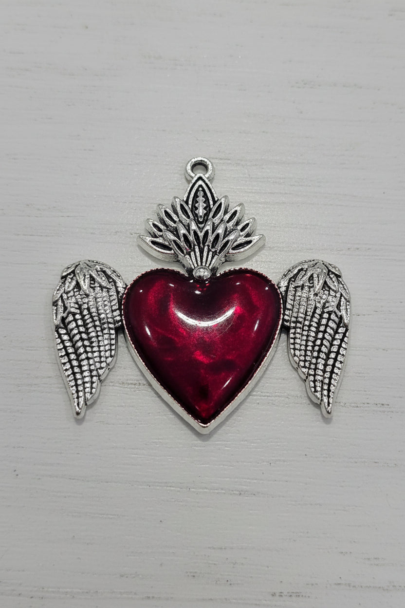 A silver-toned pendant charm featuring a central red heart with silver wings.