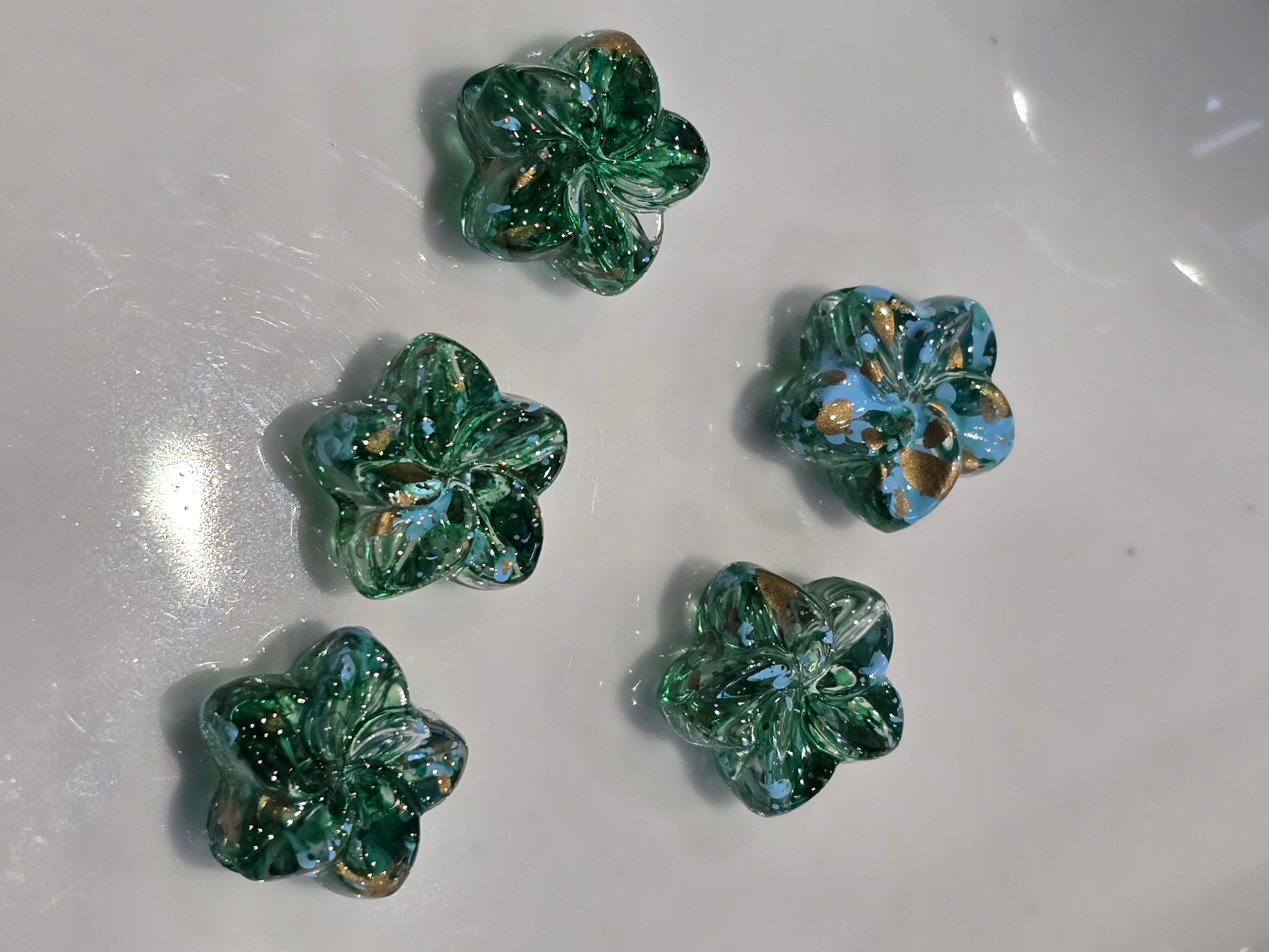 Green and blue flower-shaped acrylic beads arranged on a white surface