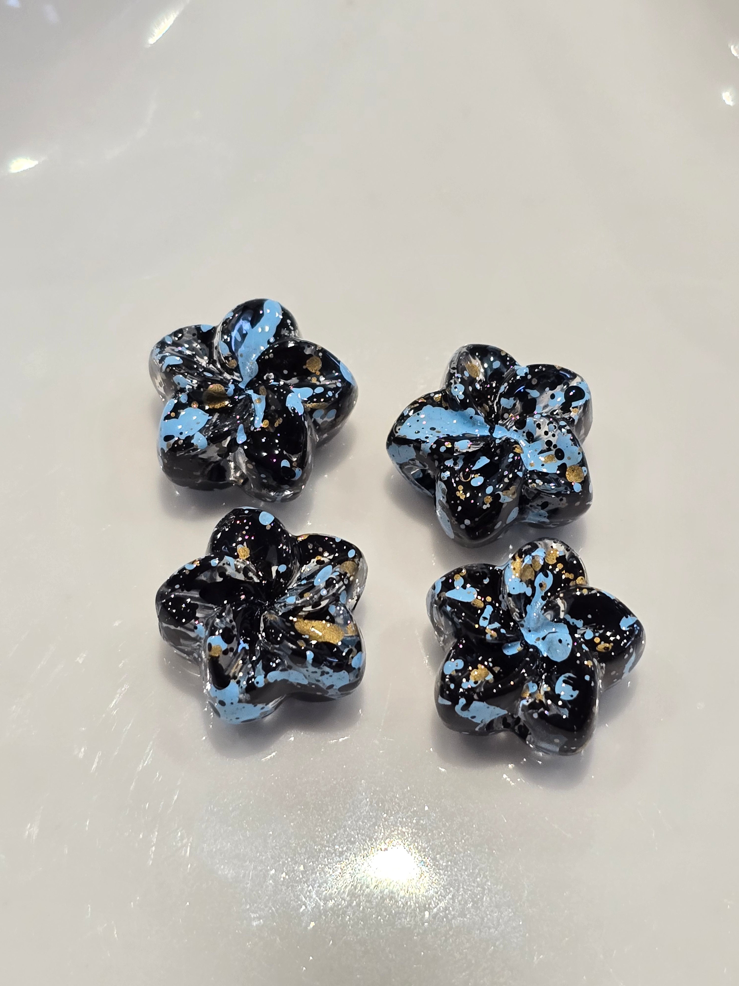 Glossy flower-shaped acrylic beads in black and light blue with gold flecks, arranged on a white surface