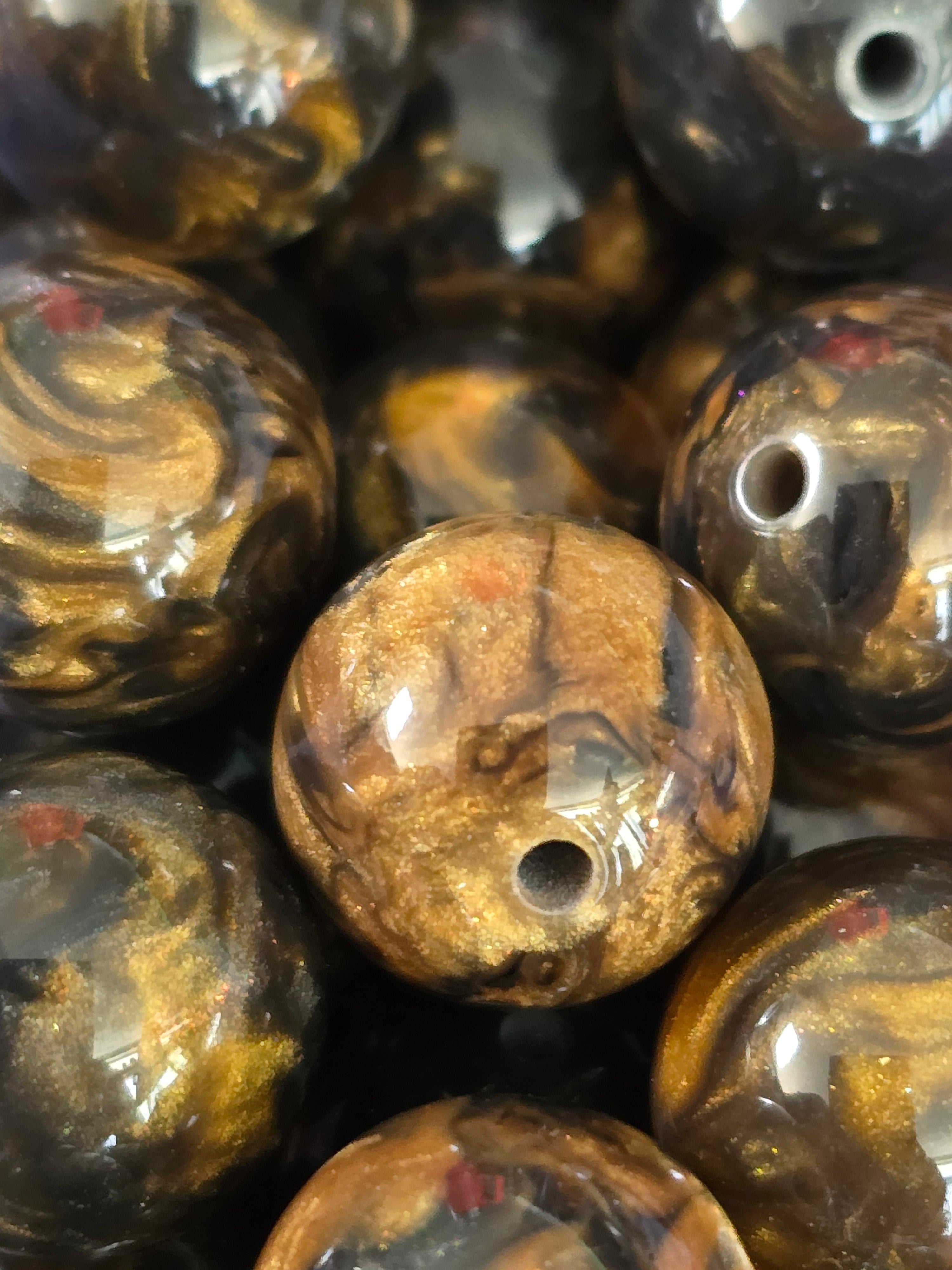 A close-up of glossy round beads with a marbled swirl pattern in brown, gold, and black.