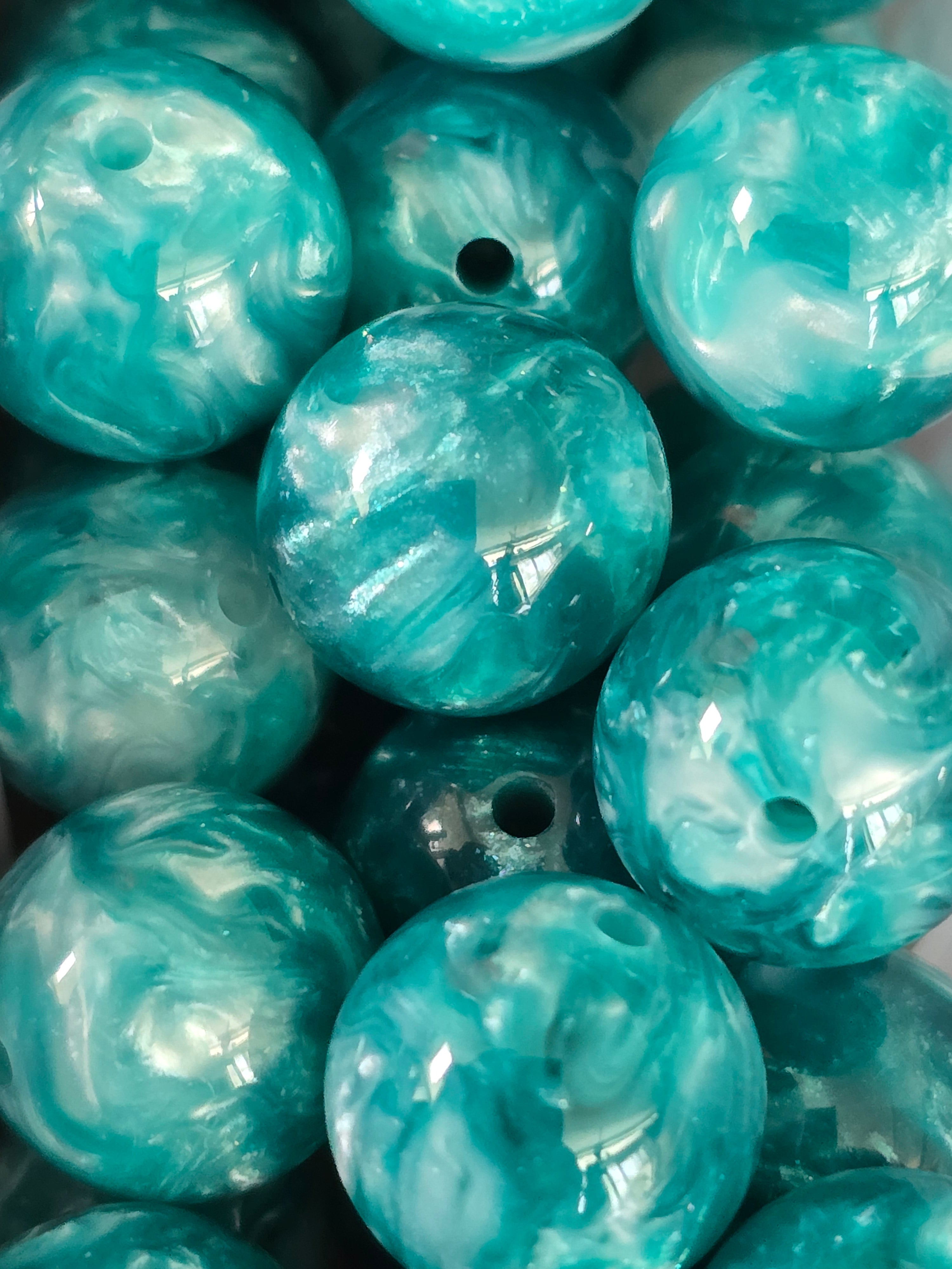 A close-up of glossy round beads with a marbled teal, aqua, and white pattern.