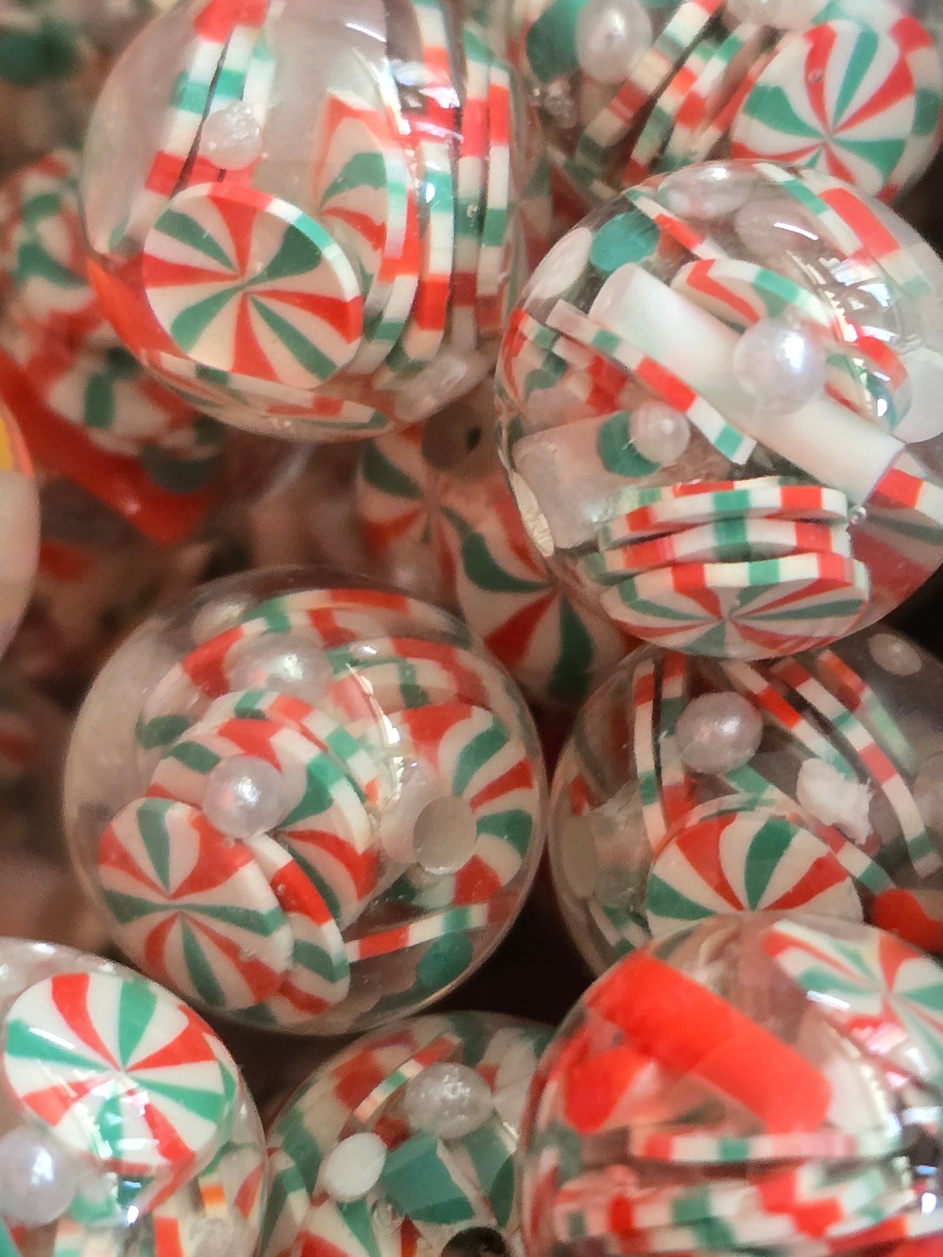 A close-up pile of clear round beads filled with red, white, and green peppermint candy pieces and small pearl-like beads.