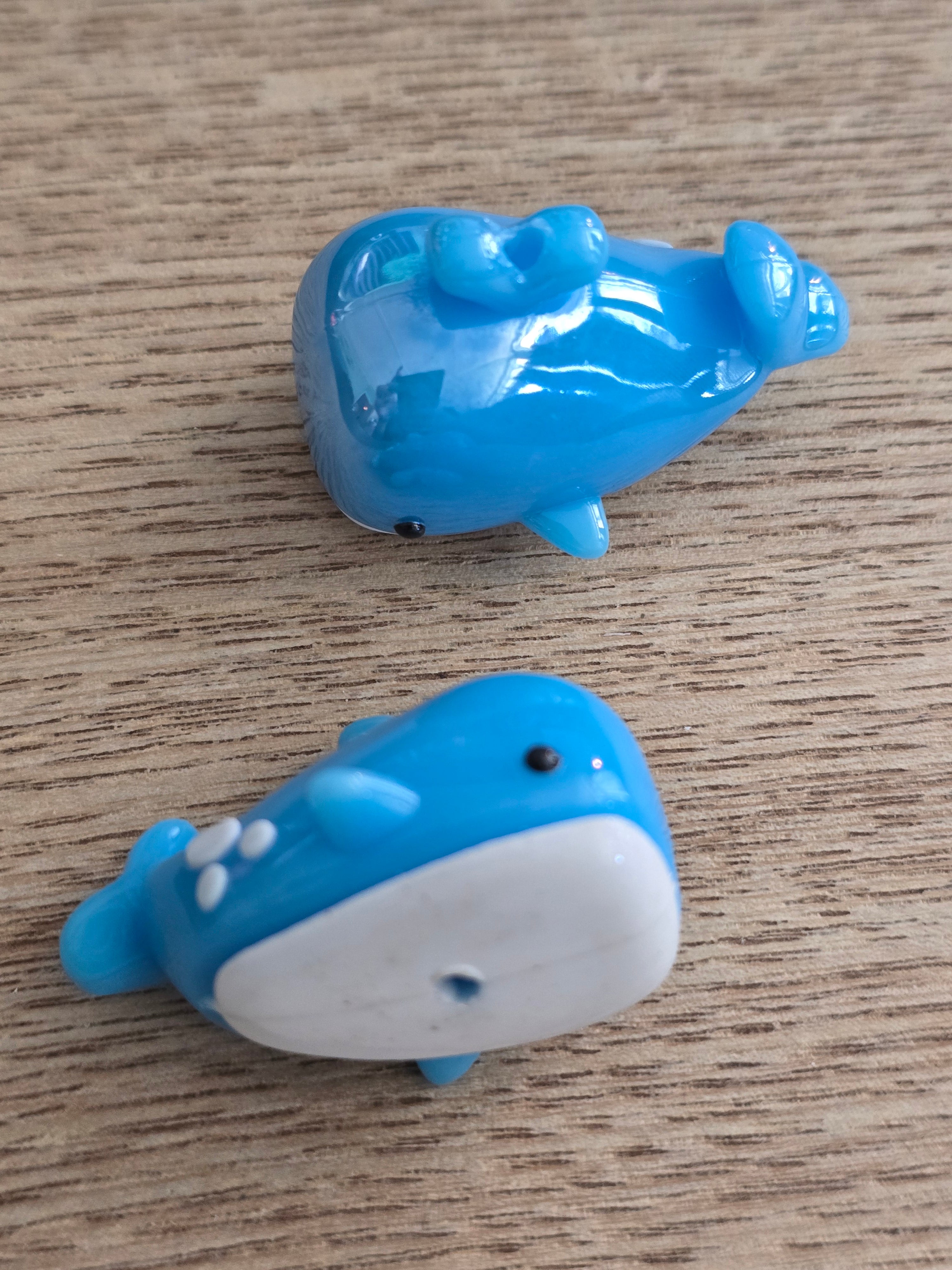 blue whale-shaped beads with one white underside and one blue underside, displayed on a light wood surface.