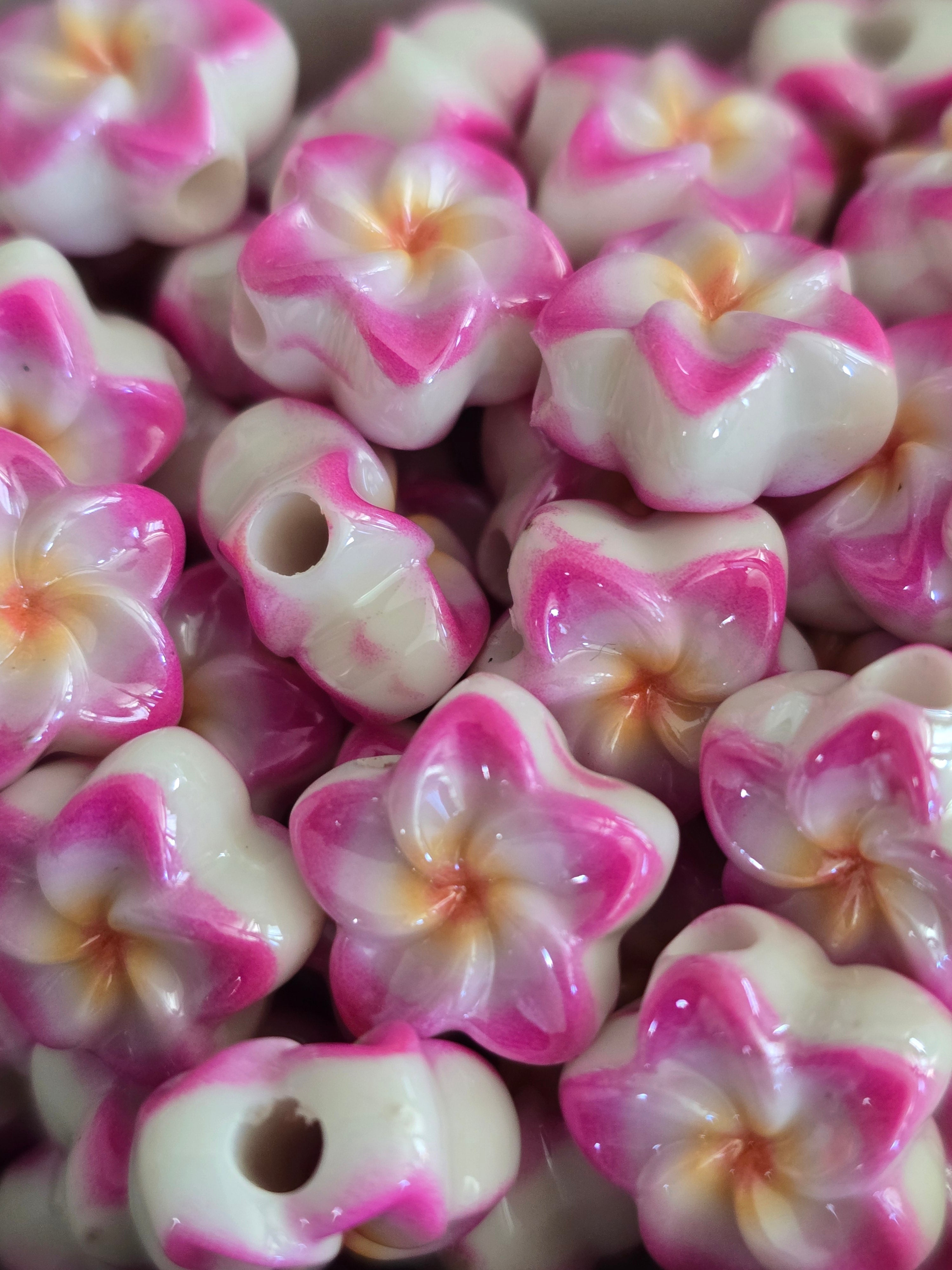 A close-up pile of glossy acrylic flower beads with white petals, pink edges, and soft peach centres.