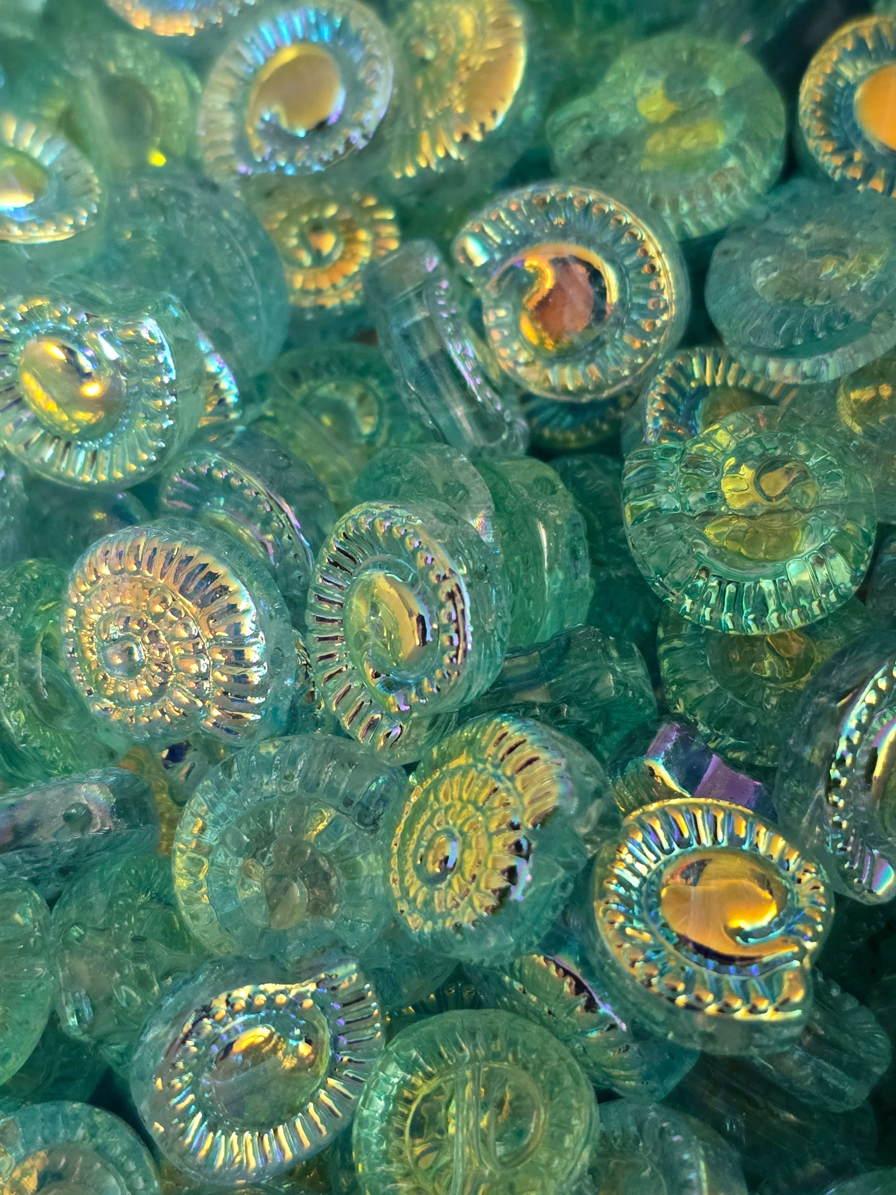 A close-up pile of round, iridescent green glass beads with a textured, ribbed outer edge and a smooth, glossy center.
