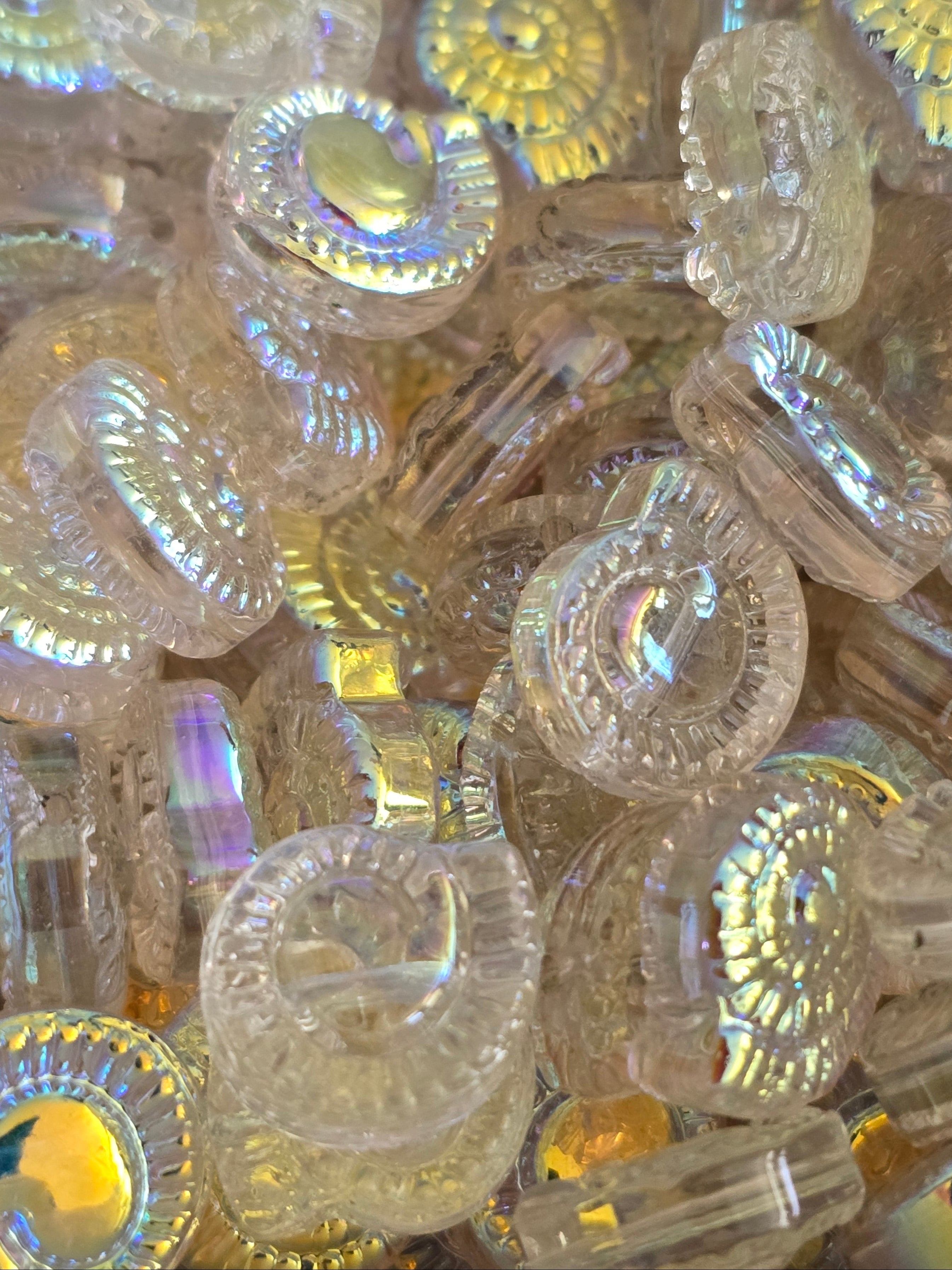 A close-up pile of small clear glass iridescent beads with gold-toned edges, showing rainbow reflections.