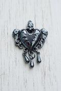 A dark metallic gothic heart pendant with skull details and dangling teardrop charms.