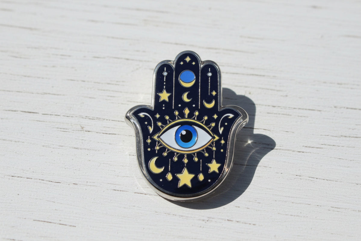 A Hamsa hand acrylic bead with a celestial design, featuring a dark blue glittery background with gold stars and crescent moons, a central blue and white eye.