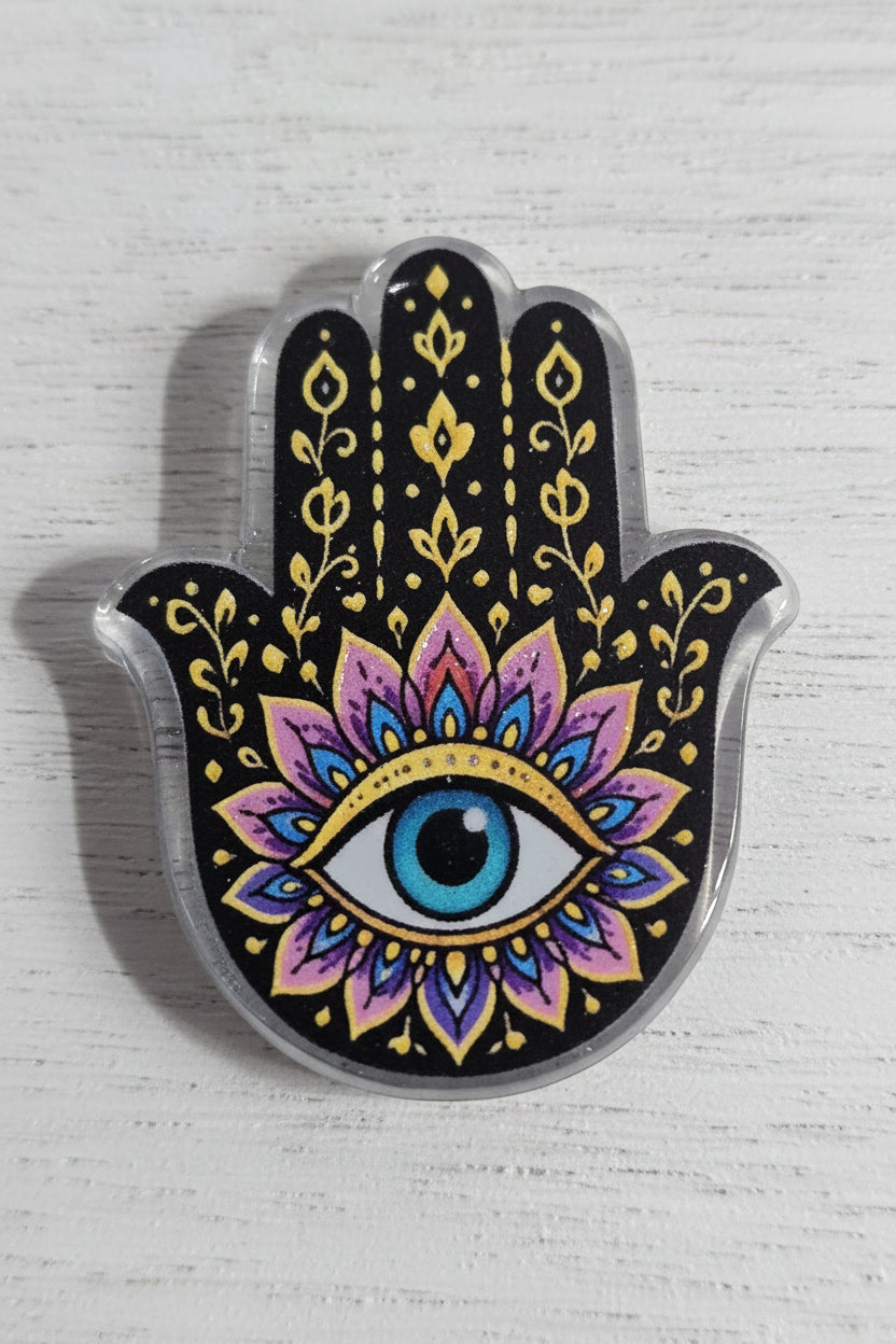 A Hamsa hand acrylic bead featuring a black background with gold filigree patterns and a central eye motif in blue, pink, purple, and white