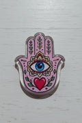 A pink Hamsa acrylic bead with a glittery silver border, featuring a blue and white eye, green leaves, a red heart, and floral patterns.