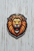 An acrylic bead depicting a roaring lion's head with a vibrant orange and yellow mane, black outlines.