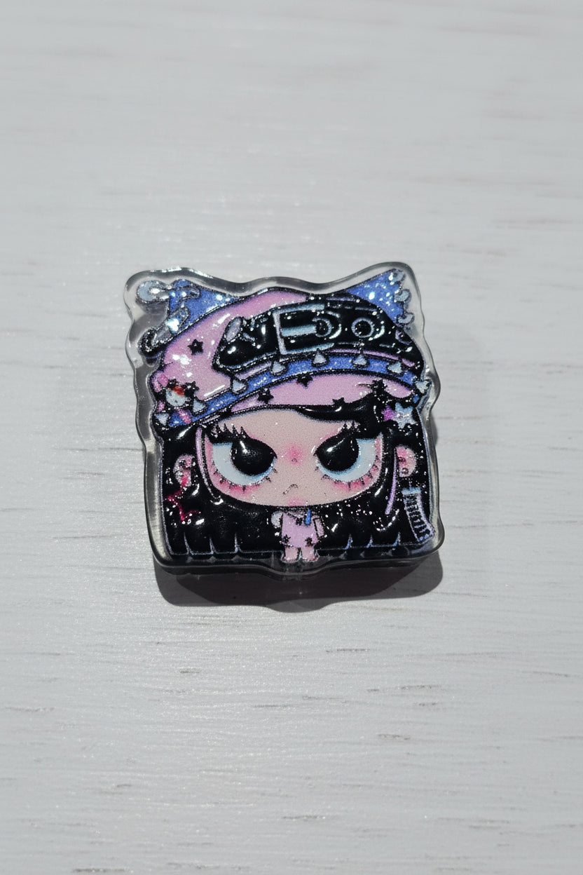 A small square bead featuring a stylized anime character with large eyes, a pink hat, and black starry details.