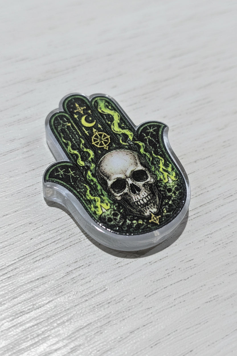 A Hamsa hand bead featuring a skull in the center with green mystical symbols and flames.