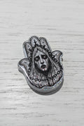 A silver-toned Hamsa hand bead featuring a detailed black and white illustration of a ghostly face with red blood at the lips.
