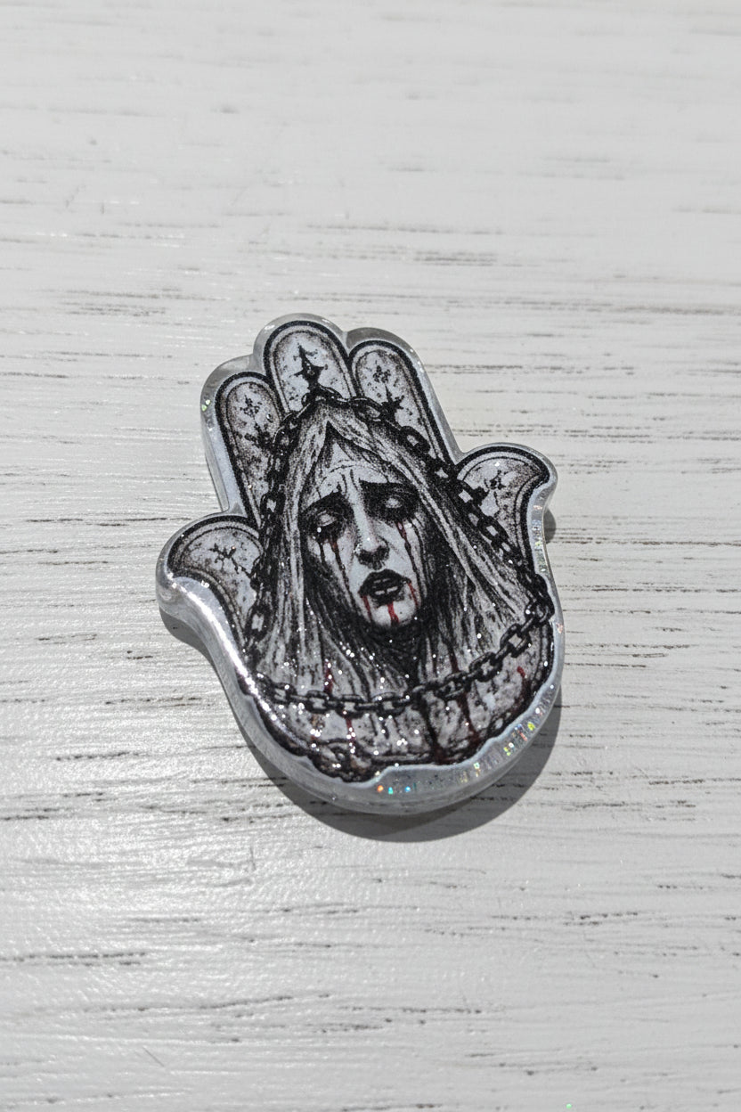 A silver-toned Hamsa hand bead featuring a detailed black and white illustration of a ghostly face with red blood at the lips.