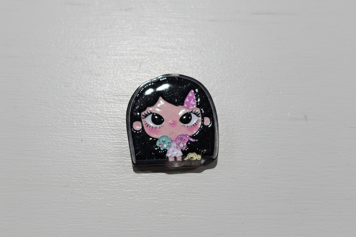 A small glossy black bead with a cartoon doll face design, featuring a pink unicorn horn and multicolored floral details.