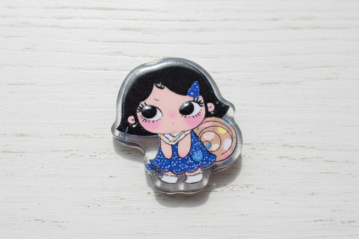 A small cartoon-style bead featuring a girl with black hair, a blue dress, and a pink face.