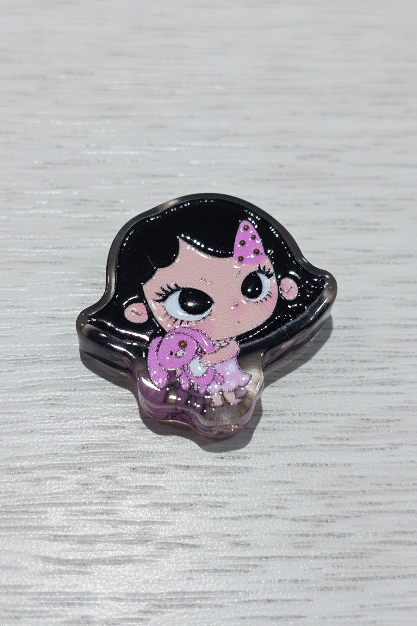 A small decorative bead featuring a cartoon girl design with black hair, large eyes, pink skin, and a pink dress.