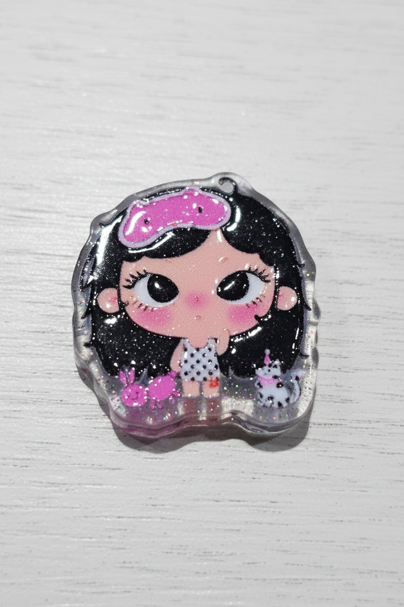 A small decorative bead featuring a cartoon girl with black hair, a pink bow, and a polka-dot dress