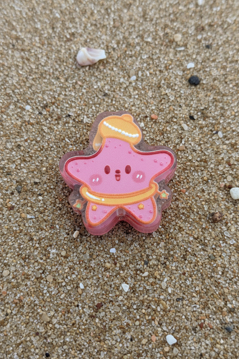 A small pink star-shaped accessory with glittery pink fill, orange trim, and a yellow top detail.