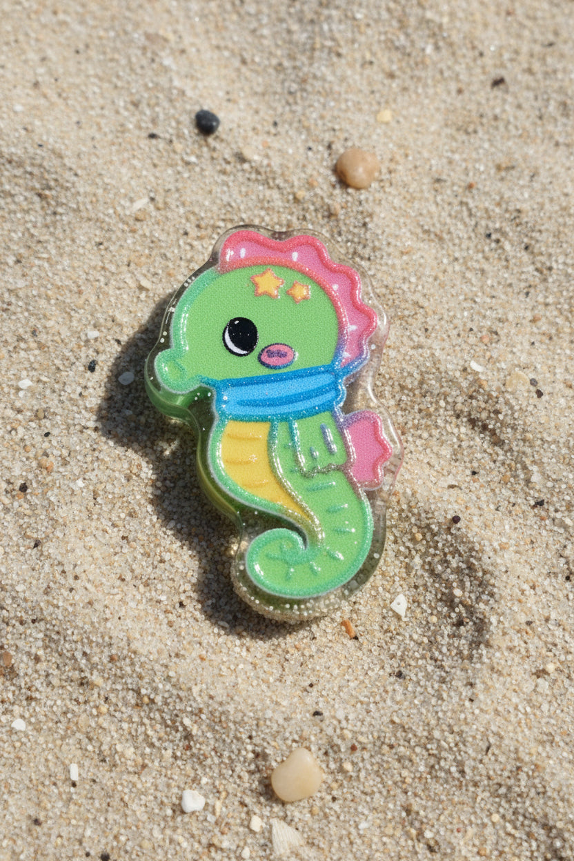 A small seahorse-shaped accessory with a green body, pink top, blue scarf, yellow belly, and black eye detail.