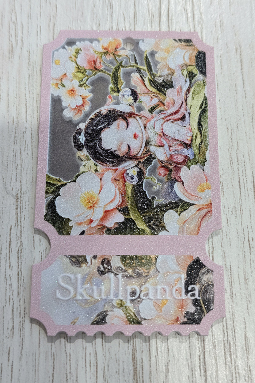 A decorative acrylic tag with a pink border and scalloped bottom edge, featuring an illustrated sleeping girl surrounded by flowers and the text 'Skullpanda' on the lower section.