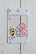 An acrylic tag featuring two chibi-style anime characters, one pink-haired figure and one blonde figure, with a crescent moon and small floral elements on a white Instagram-style card.