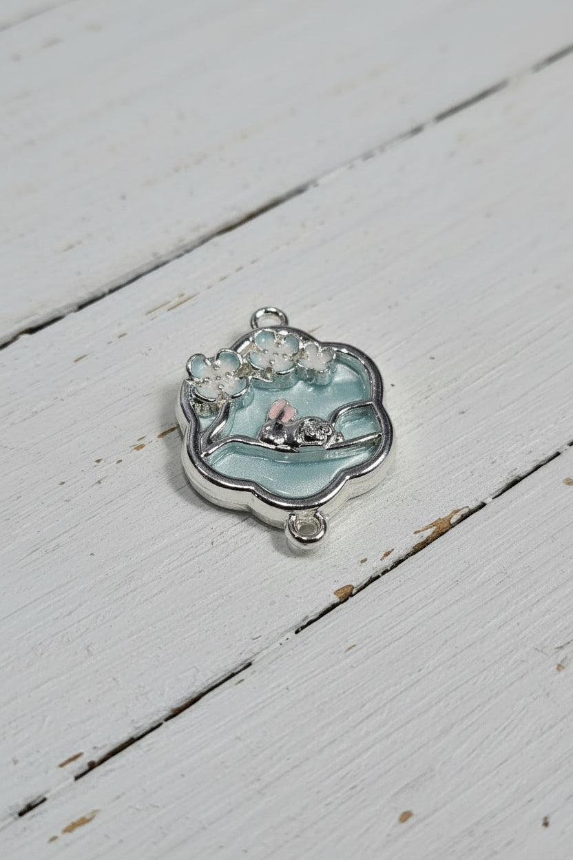 A silver-toned enamel charm featuring a small rabbit on a branch under cherry blossoms.