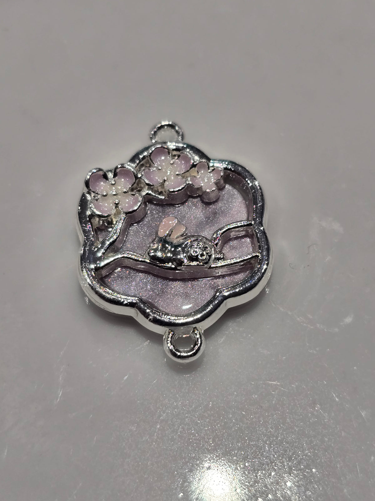A silver-toned enamel charm featuring a sleeping bunny under purple cherry blossoms.