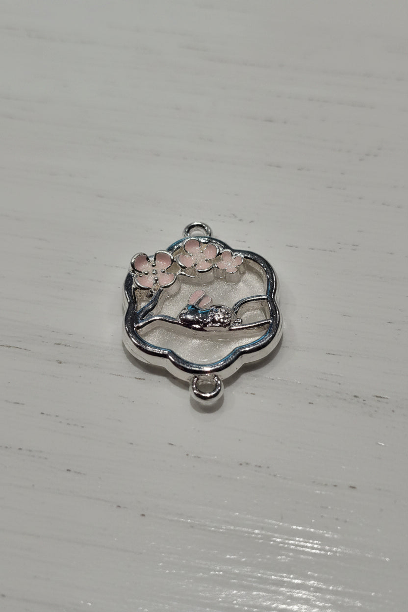A silver-toned floral and bunny charm pendant with pink enamel details.