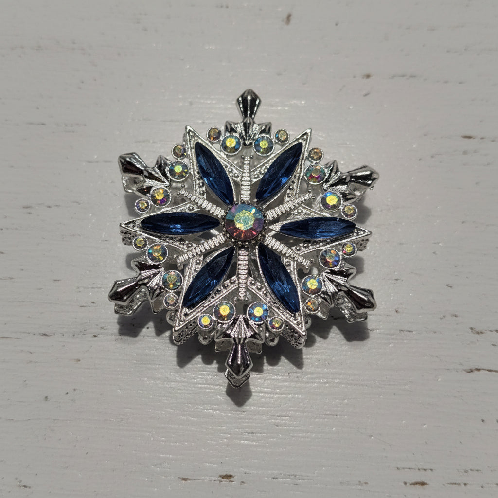 A snowflake-shaped bead featuring dark blue marquise-cut crystals, a small iridescent center crystal, and silver-toned metal with clear rhinestones