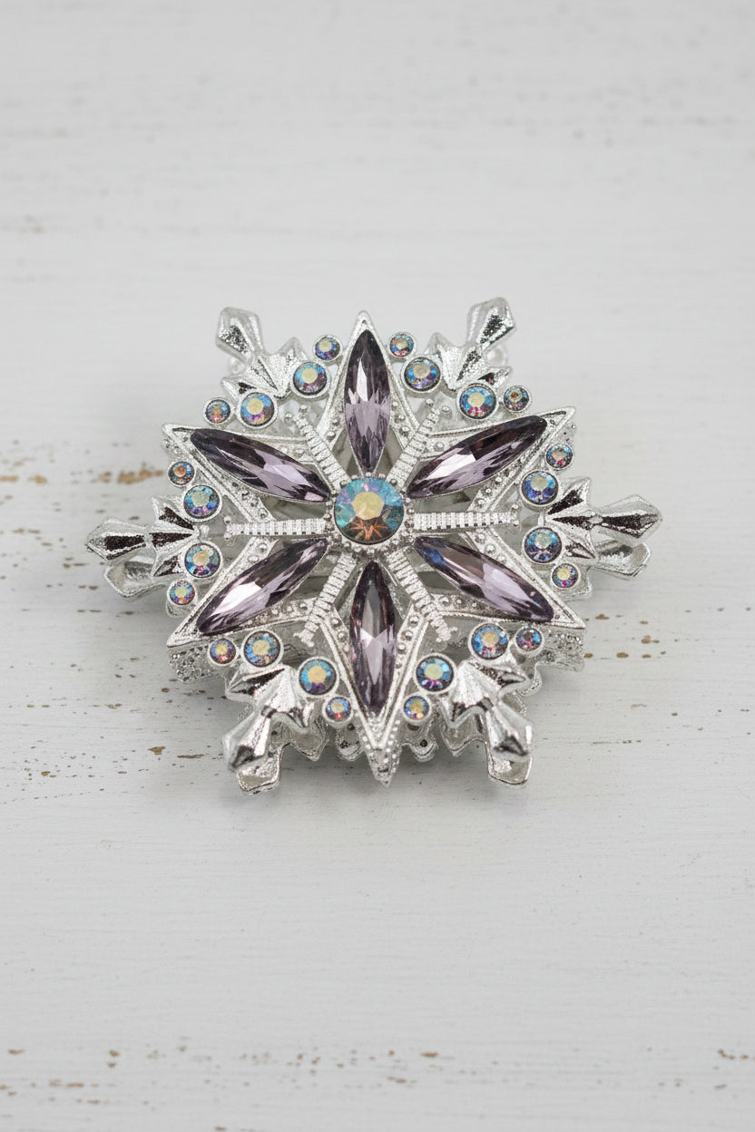 A snowflake-shaped bead featuring silver-toned metalwork, clear faceted crystals, and lavender-purple marquise crystals, with an iridescent center stone.