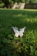 A butterfly-shaped jewellery charm with light pink enamel, silver-toned metal borders, and a small green accent near the centre.