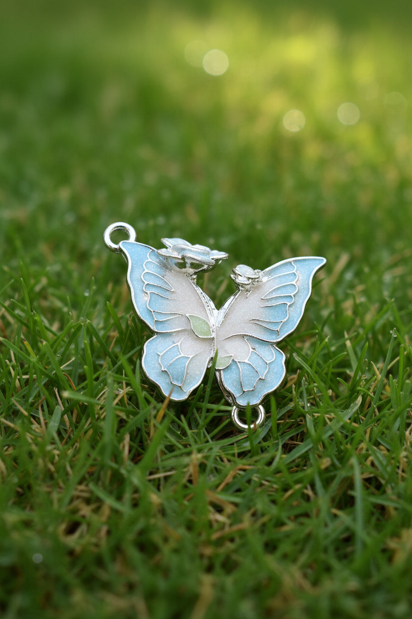 A butterfly-shaped jewellery charm with iridescent light blue and white enamel, outlined in silver-tone metal.