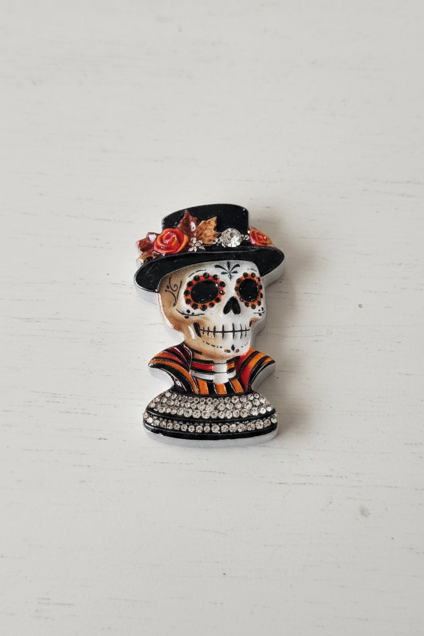 A Day of the Dead sugar skull bead with a black top hat adorned with red and orange flowers, wearing a striped black, orange, and red collar.