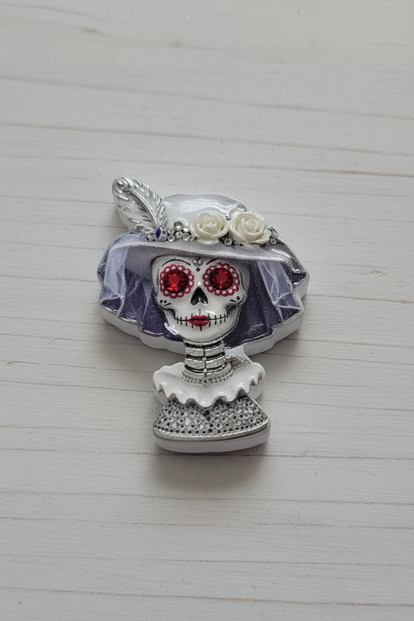 A Day of the Dead sugar skull bead  featuring red eyes, a white veil, and a feather detail.