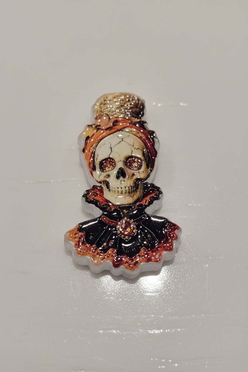 A small decorative skull bead with a black ruffled collar, and orange-red trim.