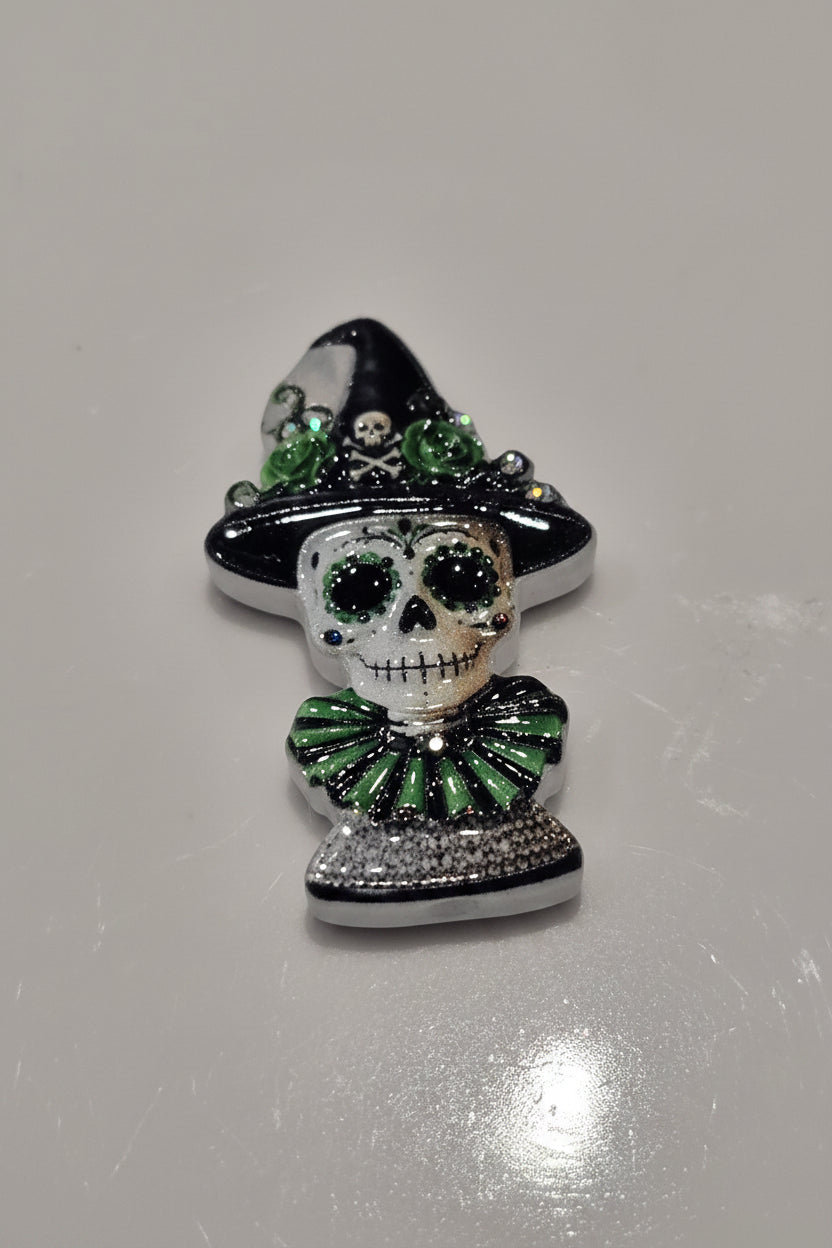 A Day of the Dead sugar skull bead wearing a black witch hat and a green ruffled collar.