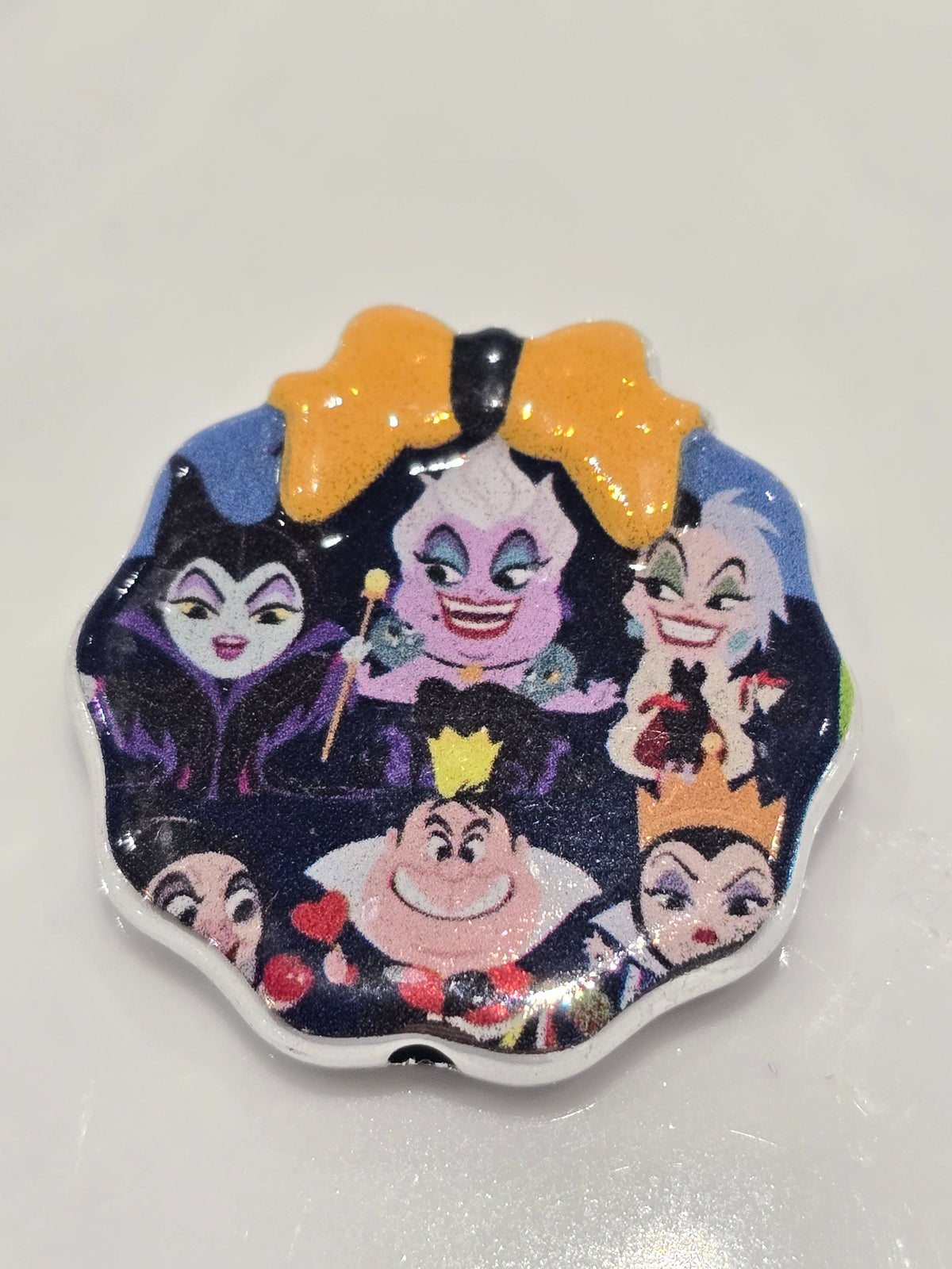A scalloped-edge bead bearing a colorful printed design of Disney's Maleficent and other classic princess characters on a dark background, with a large orange bow at the top.