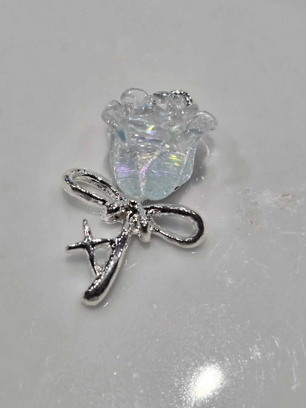 A small jewelry charm featuring a silver-toned bow with a clear, iridescent, flower-shape.