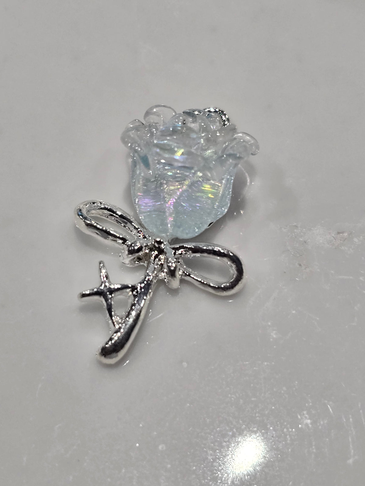 A small jewelry charm featuring a silver-toned bow with a clear, iridescent, flower-shape.