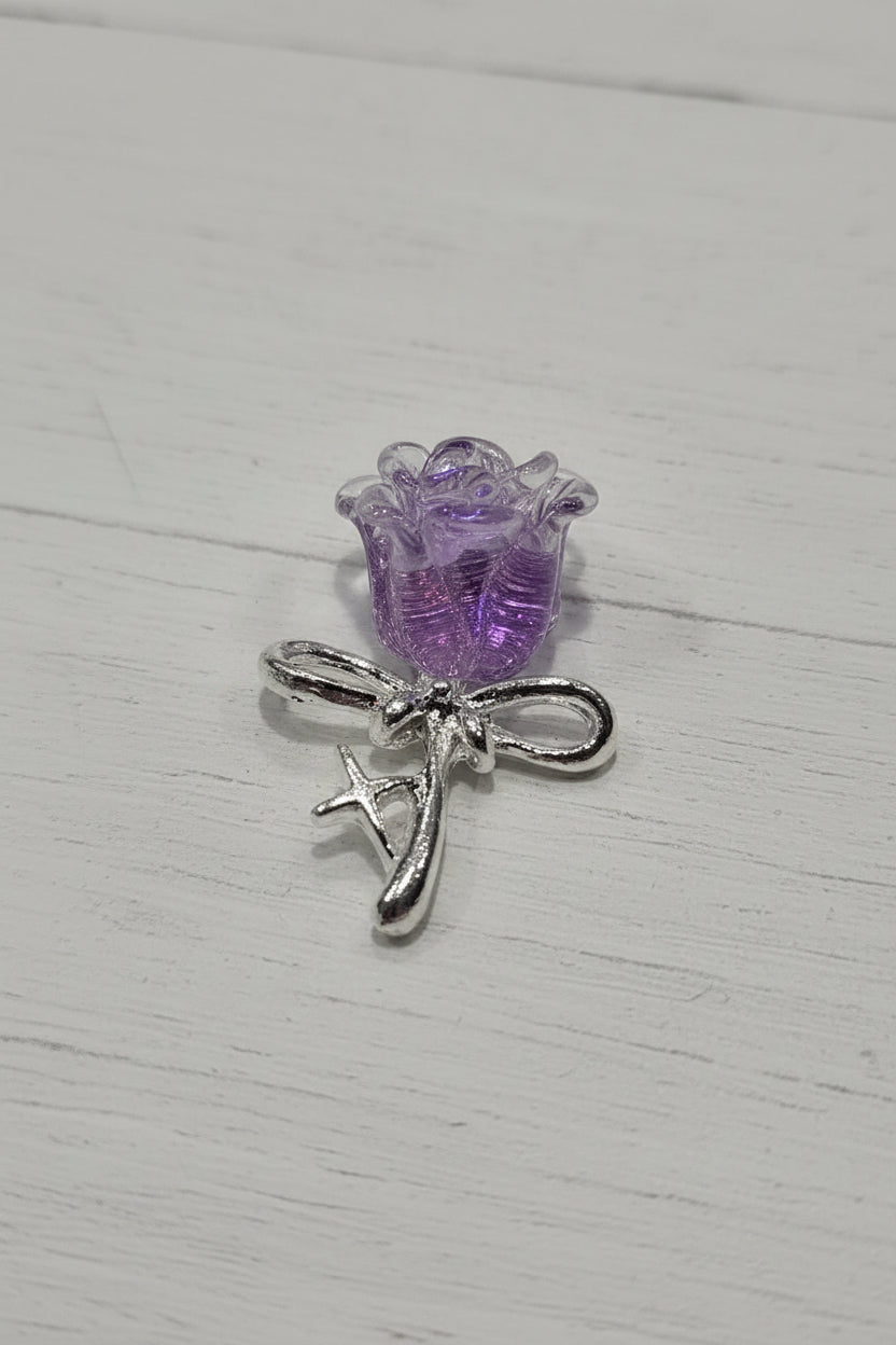 A small jewelry charm featuring a textured purple glittery flower bud attached to a silver-tone metal loop and decorative letter detail.