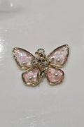 A butterfly-shaped charm featuring iridescent pink wings with pearl-like accents and a gold-tone body and borders.