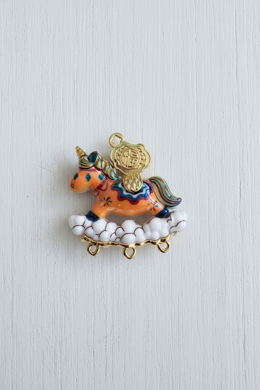 A colorful resin unicorn pendant with gold-tone metal details, resting on a white cloud base.