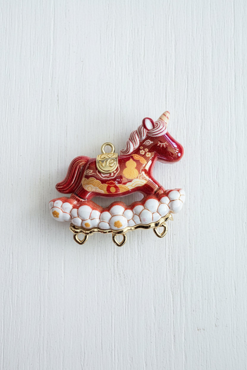A decorative unicorn resin pendant with a red and pink unicorn, white cloud-like base, and gold accents.