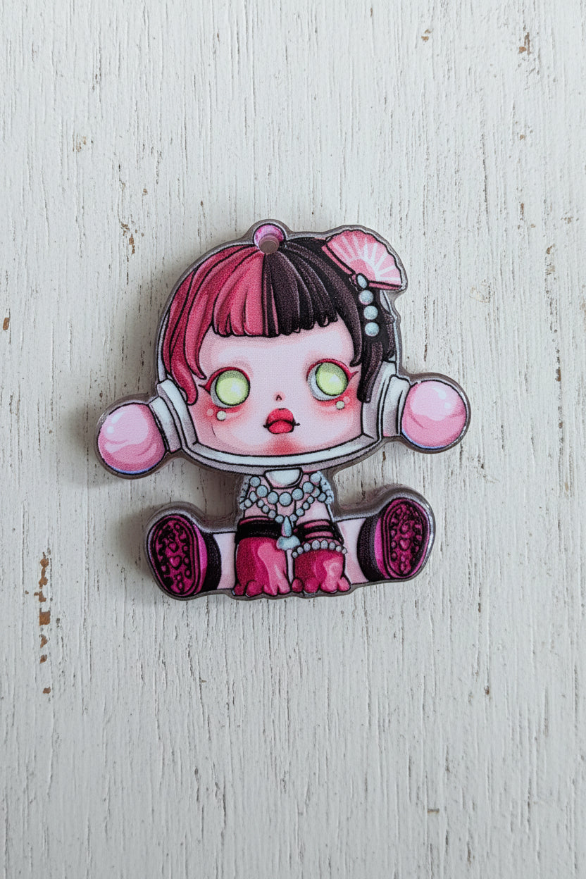 A cartoon-style acrylic bead of a girl with pink and black hair, glowing green eyes.