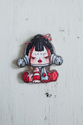 An acrylic bead featuring a stylized anime character with black hair, red and white clothing, and gray mechanical-looking accessories.
